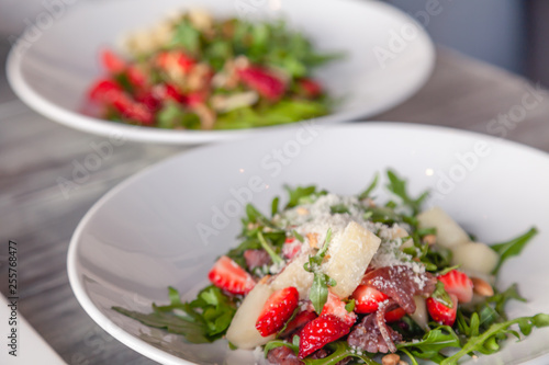 Close-up fresh summer salad with basturma jerky, greens, arugula, strawberries, melon, parmesan cheese. Concept delicacy, new menu in trendy restaurant