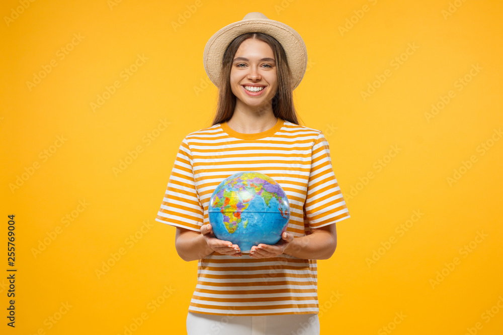 Travel concept. Young female tourist holding globe with both hands, isolated on yellow background Travel concept. Young female tourist holding globe with both hands, isolated on yellow background