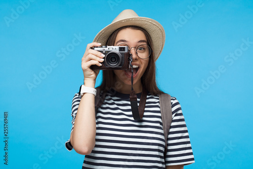 Smiling young girl tourist holding camera, isolated on blue background