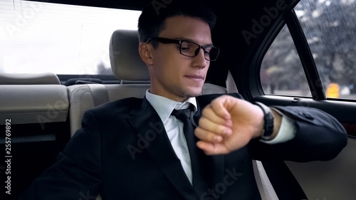 Young anxious businessman late for flight, looking at watch, traffic in city © motortion
