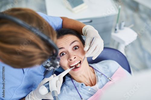 Young woman being terrified during dental procedure at clinic
