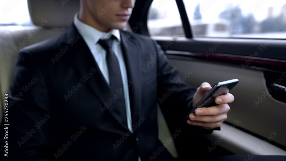 Young male in suit texting on smartphone while riding in personal business car Young male in suit texting on smartphone while riding in personal business car