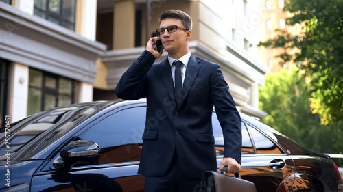Businessman standing near luxurious car talking on smartphone, unhappy with news © motortion