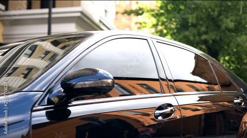 Luksusowy samochód z przyciemnianym szkłem stojący na parkingu, odbicie biznesmena