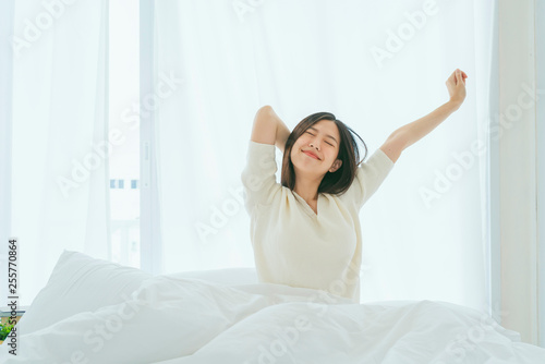 white dress asian beautiful woman stretching morning wake up bedroom with white curtain background lifestyle home concept