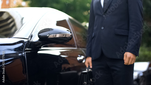 Premium class driver standing near luxury car, work for refugees, service