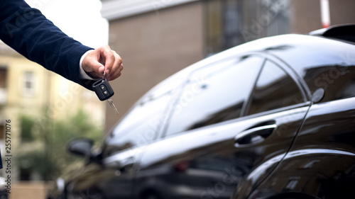 Salesman giving car key to buyer, dealership showroom, auto rental, luxury
