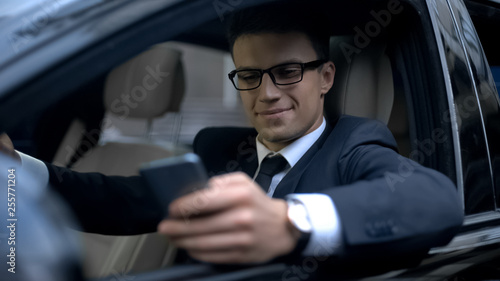 Glad businessman texting with girlfriend and smiling, sitting in car, smartphone © motortion