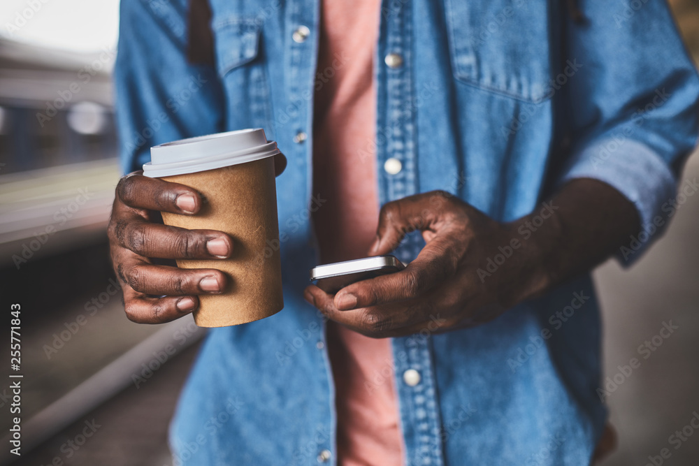 Afro-american man holding paper glass of cofee and using smartphone Afro-american man holding paper glass of cofee and using smartphone