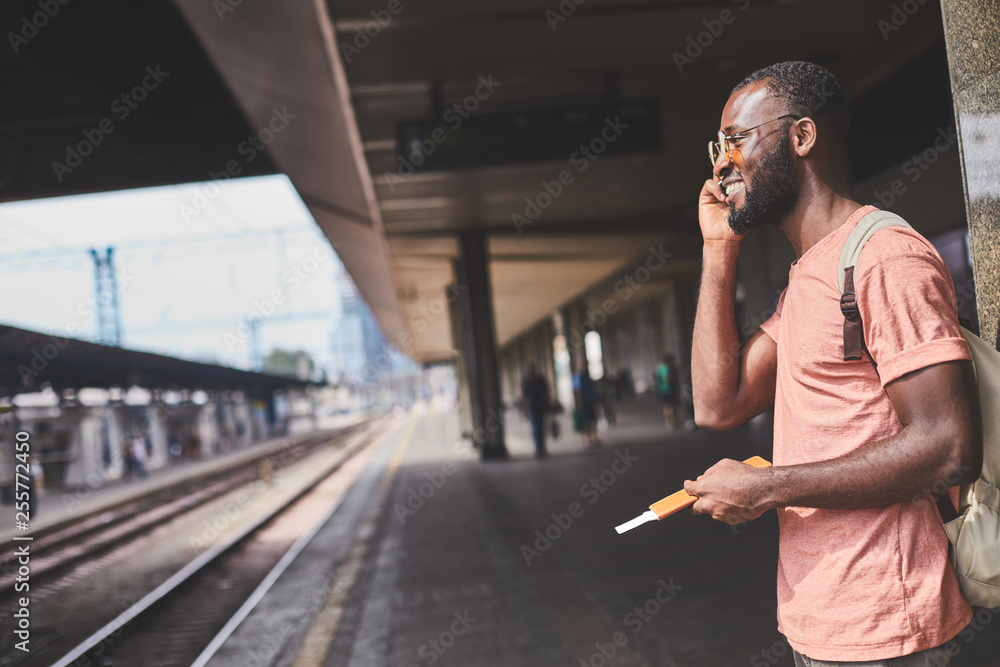 Fototapeta premium Afro-american man standing on station and using mobile phone
