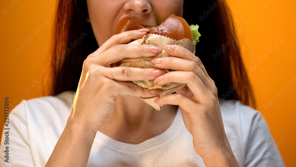 Woman eagerly eating tasty cheeseburger, bad eating habits, unhealthy snack Woman eagerly eating tasty cheeseburger, bad eating habits, unhealthy snack
