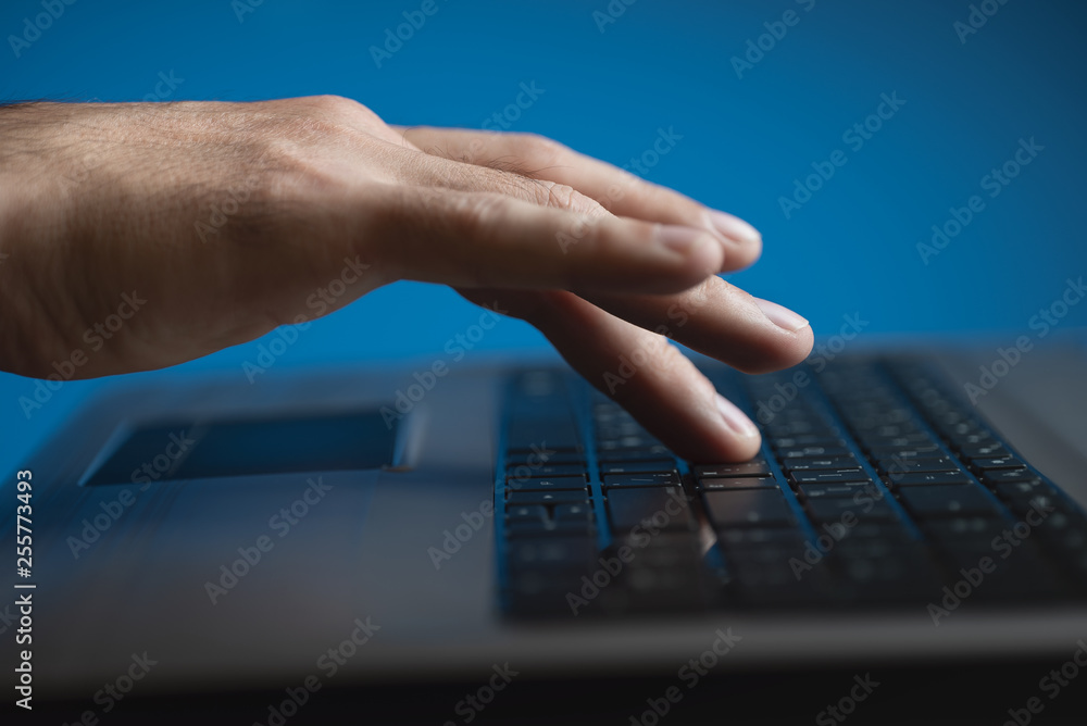 Men's hand and laptop keyboard. Blue background Men's hand and laptop keyboard. Blue background