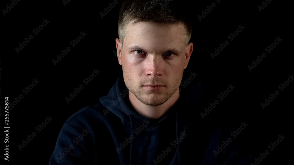 Obraz premium Serious male looking into camera, sitting on black background, close up view