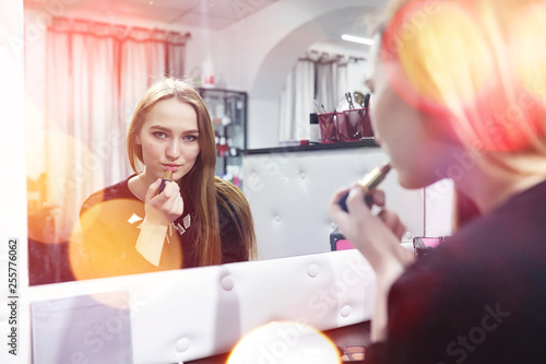 A young girl does make-up in a beauty salon. The girl in front of the mirror is making up. Beauty saloon.