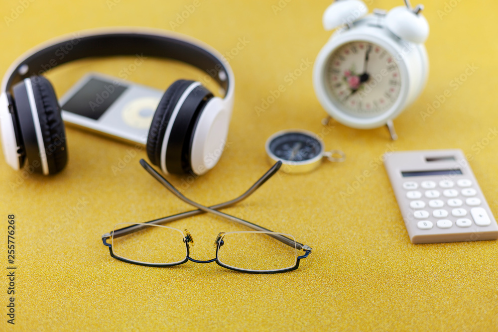 Headphone with white alarm clock,compass and calculator on gold glitter texture sparkling shiny paper background Headphone with white alarm clock,compass and calculator on gold glitter texture sparkling shiny paper background