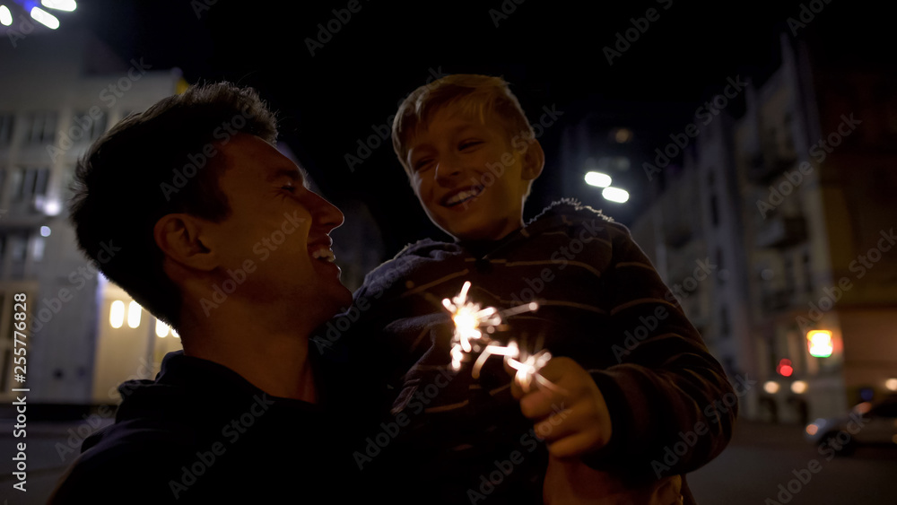 Guy holding younger brother in hands, burning bengal light, celebrating birthday Guy holding younger brother in hands, burning bengal light, celebrating birthday