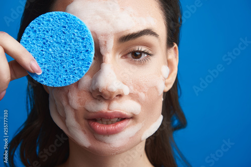 Young woman closing eye with cosmetic sponge