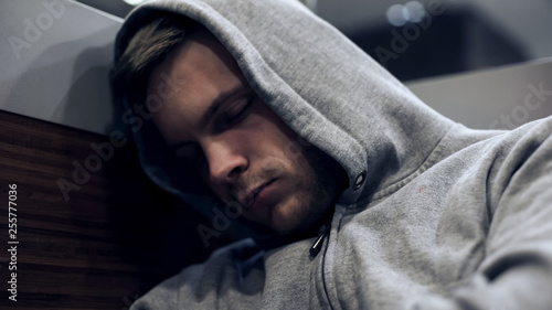 Homeless man in hoodie sleeping in public transport, unemployment problems