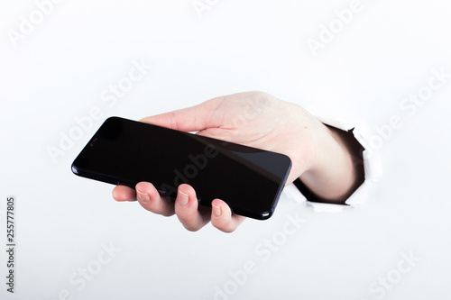 Female hand out of the hole in the paperman, holding a smartphone with a black screen. Isolate on white background. photo