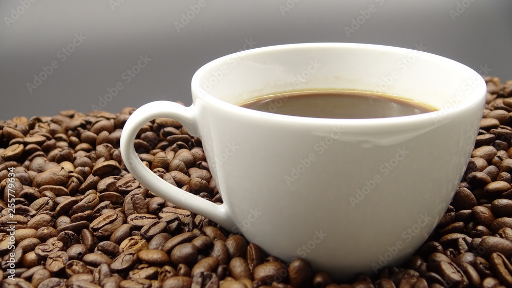 A cup of black coffee over roasted coffee beans A cup of black coffee over roasted coffee beans