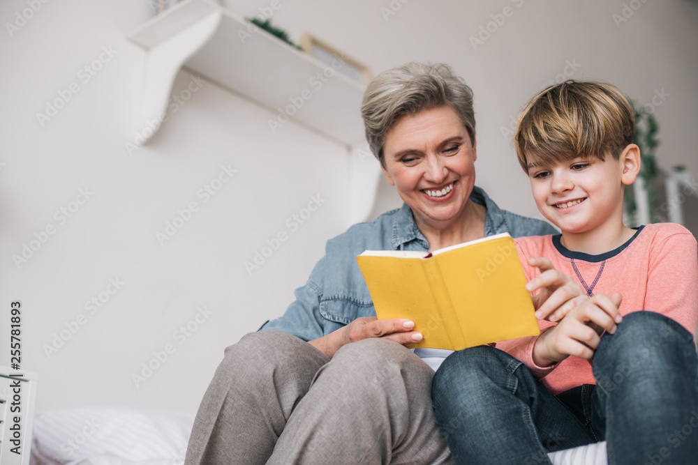 Low angle of little boy reading book with his grandmother in house Low angle of little boy reading book with his grandmother in house