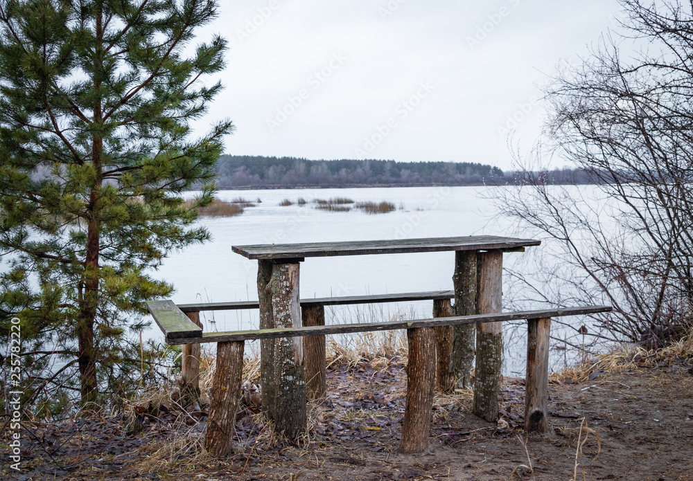 wooden table for outdoor recreation on the river bank in spring in March, waiting for visitors.