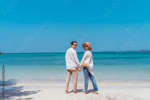 Young happy muslim couple white dress on seashore. Travel Vacation Retirement Lifestyle Concept. young couple holding hands and turn back on the beach in vacation day. summer time.