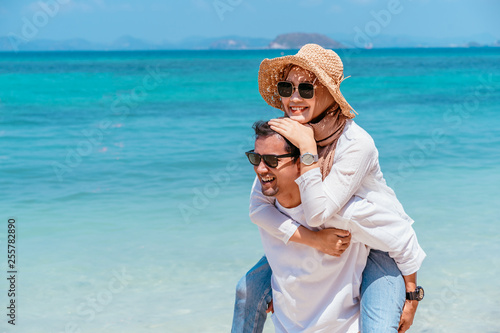 Young happy muslim couple white dress on seashore. Travel Vacation Retirement Lifestyle Concept. Man giving piggyback ride to girlfriend on the beach on the beach in vacation day. summer time.