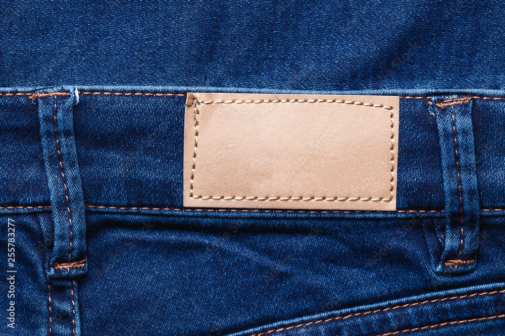 Brown leather empty copy space label texture. Back side of blue denim jeans trousers background.	
