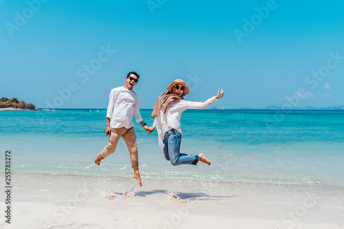 Young happy muslim couple white dress on seashore. Travel Vacation Retirement Lifestyle Concept. young couple jumping on the beach in vacation day. summer time.
