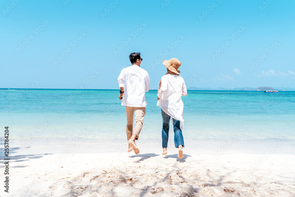 Young happy muslim couple white dress on seashore. Travel Vacation Retirement Lifestyle Concept. young couple holding hands and turn back on the beach in vacation day. summer time.