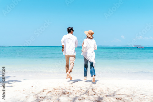 Young happy muslim couple white dress on seashore. Travel Vacation Retirement Lifestyle Concept. young couple holding hands and turn back on the beach in vacation day. summer time.