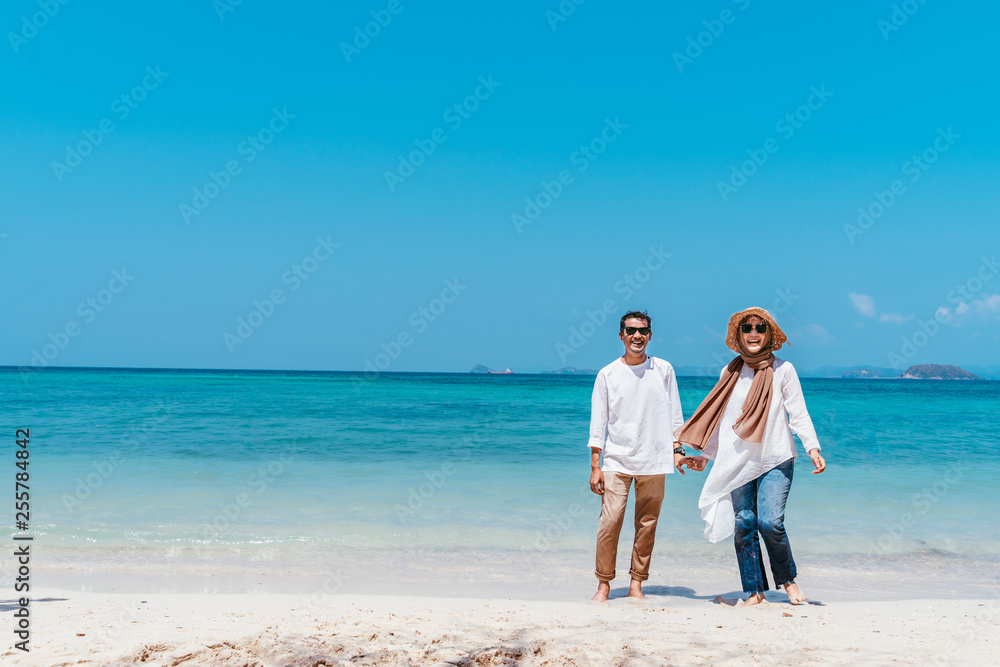 Young happy muslim couple white dress on seashore. Travel Vacation Retirement Lifestyle Concept. young couple holding hands on the beach in vacation day. summer time.
