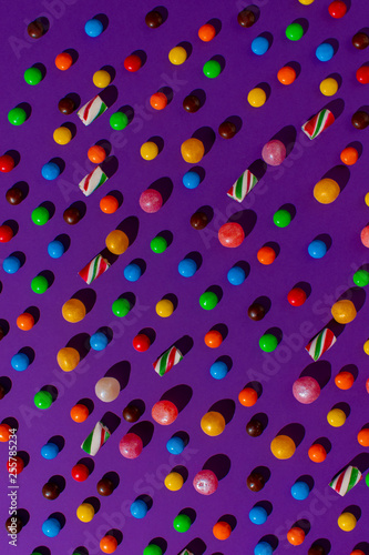 bright candy scattered on a flat purple background. View from above.