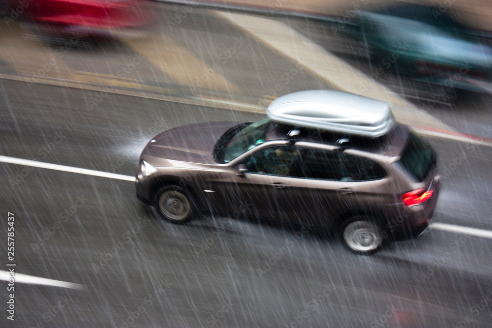 Rainy day in the city: A driving car in the street hit by the heavy rain with hail, in motion blur