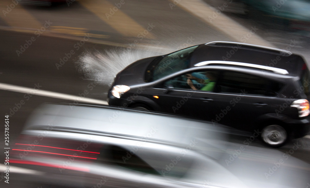 Rainy day in the city: Driving cars in the street, splashing water, in motion blur