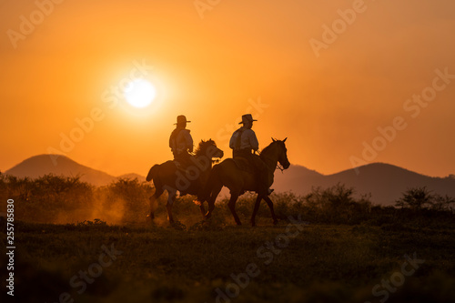 silhouette two cowboys ride with they horses under sunset