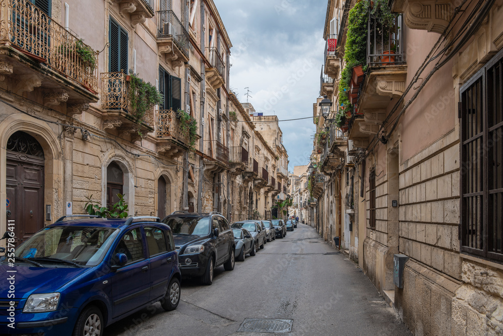 Typical italian narrow street with cars in the row in the island of Ortigia, Syracuse, Sicily, Italy