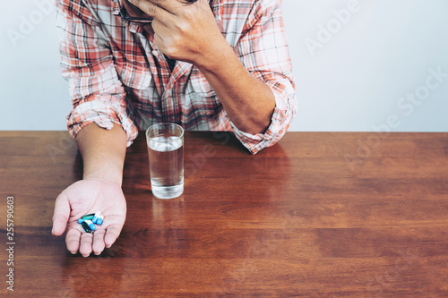 Extremely tired.man holding pill and glass of water in hands taking emergency medicine in office, meds side effects concept, close up view