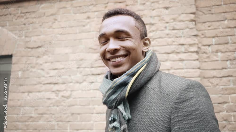 Portrait shot of handsome smiling, winking and saying yes African American man in a coat and a scarf. Handheld slow motion shot Portrait shot of handsome smiling, winking and saying yes African American man in a coat and a scarf. Handheld slow motion shot