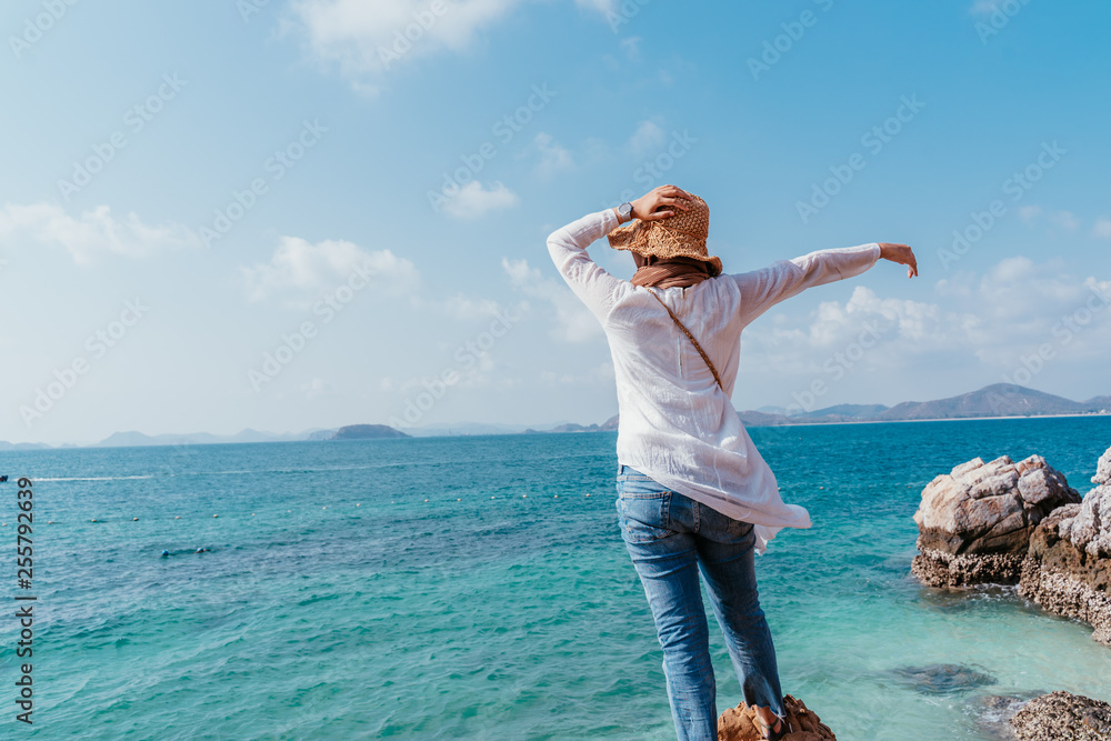 Back view of young asian woman looking from cliff. Future and research concept. Woman with hands up standing on cliff over sea. Travel concept, concepts of winner, freedom