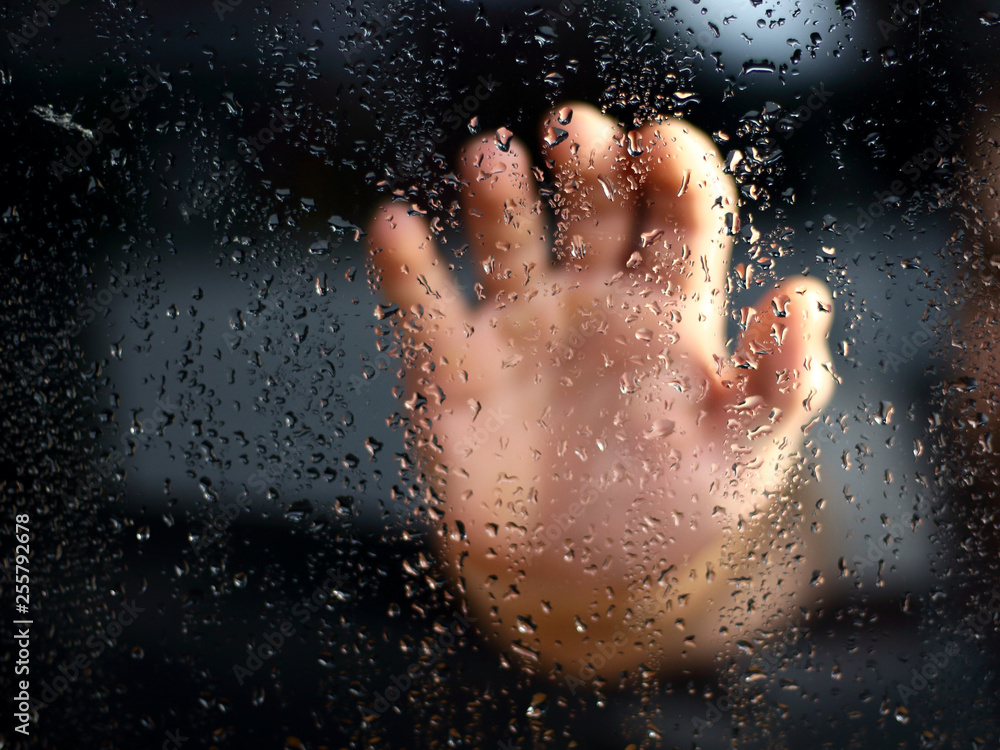 Male hand palm silhouette through the window with raindrops reaching for the glass. A request for help, depression blurred bokeh background