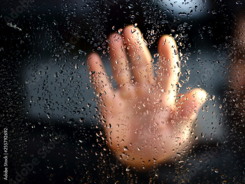 Male hand palm silhouette through behind the window with raindrops reaching for the glass. A request for help  depression blurred bokeh background. Refusal  denial of alcohol and drugs