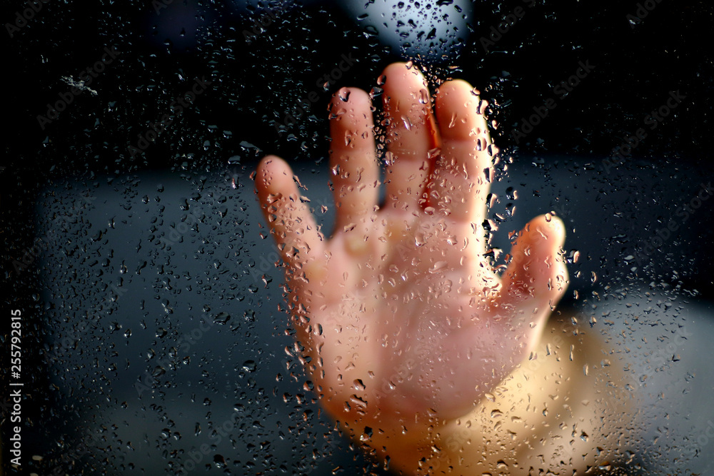 Fototapeta premium Male hand palm silhouette through the window with raindrops reaching for the glass. A request for help, depression blurred bokeh background
