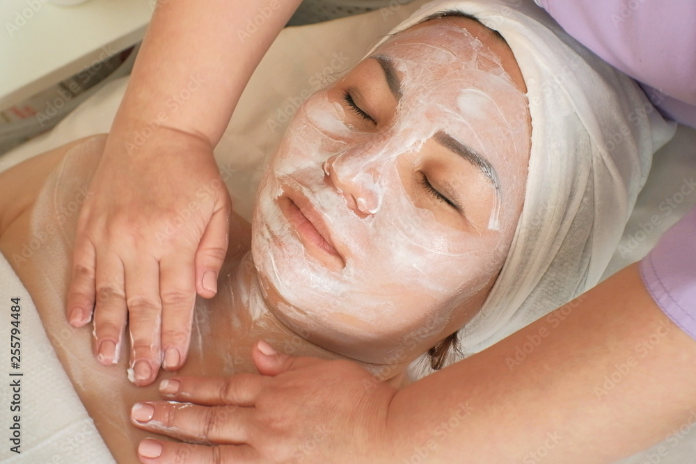 A cosmetologist massages a woman's face and neck with a moisturizing mask. Close-up. Relaxed Asian woman takes beauty treatments in the beauty salon. Cosmetology. Beauty