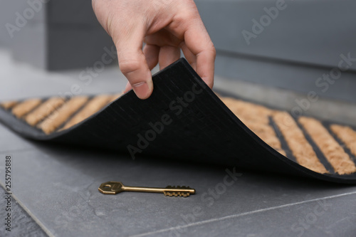 Man lifting door mat and finding hidden key, closeup view photo