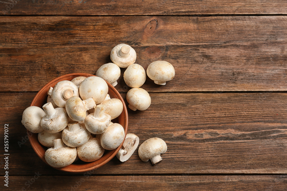 Bowl of fresh champignon mushrooms on wooden background, top view with space for text Bowl of fresh champignon mushrooms on wooden background, top view with space for text