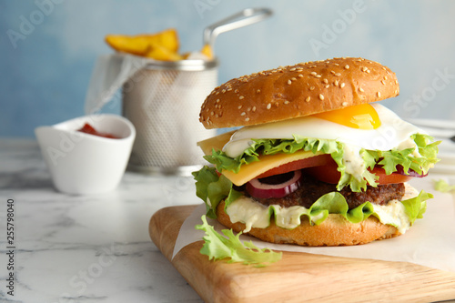 Tasty burger with fried egg on wooden board  space for text