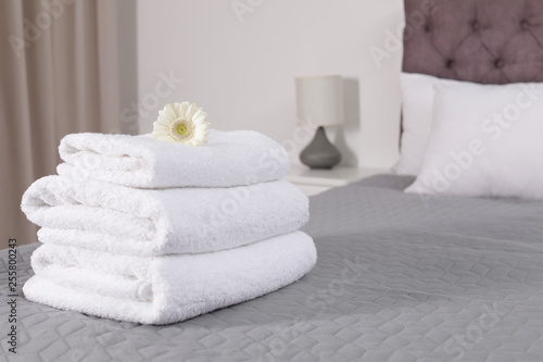 Stack of fresh towels with flower on bed in hotel room