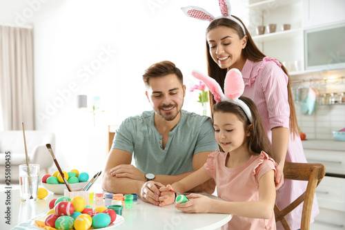 Father, mother and daughter painting Easter eggs in kitchen, space for text